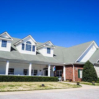 A large suburban house with a green roof and brick accents under a clear blue sky.