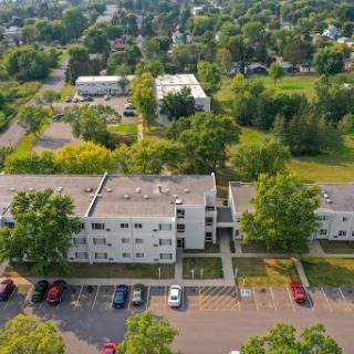 An aerial view of a residential apartment complex surrounded by greenery and parked cars.