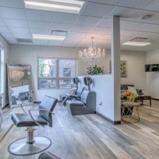 A cozy salon interior with styling stations, chairs, and a chandelier.