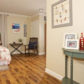 A cozy bedroom with wooden flooring, decorated with wall art and simple furniture.