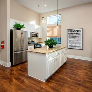 A modern kitchen featuring stainless steel appliances, a large island with pendant lighting, and wood flooring.