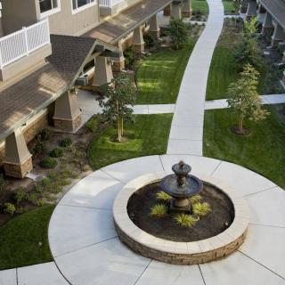 A beautifully landscaped courtyard featuring a central fountain and winding pathways connecting the apartment units.