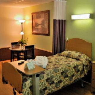 A cozy hospital room with a single bed, bedside table, and a small dining area.