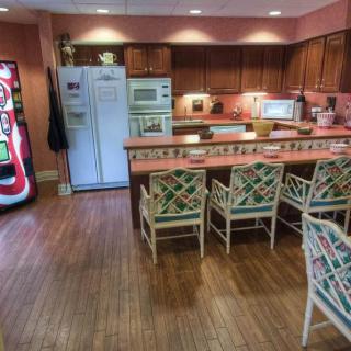 A spacious kitchen with a bar counter and chairs, featuring wooden cabinets and flooring, along with a refrigerator and a vending machine.