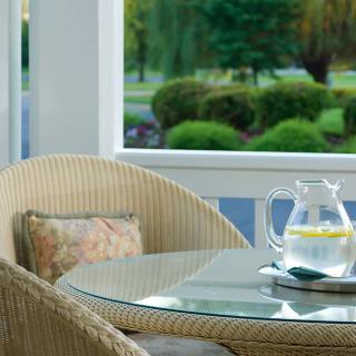 A cozy patio setting with a glass table, wicker chair, and a pitcher of lemon water.