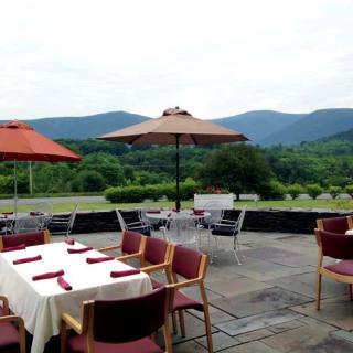 A picturesque outdoor dining area set against a backdrop of rolling mountains with neatly arranged tables and umbrellas.
