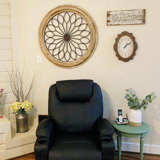 A cozy living room corner featuring a black recliner, wall art, and a side table with plants.