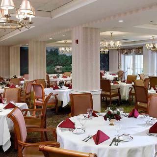 An elegant dining room with neatly set tables and chandeliers overhead.