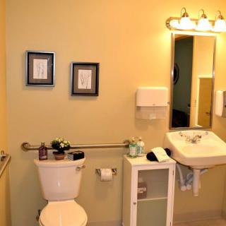 A well-organized bathroom featuring a sink, mirror, and toilet with wall decorations and lighting.