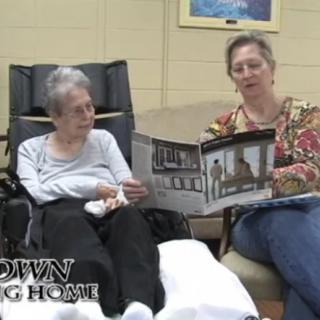An elderly woman and a caregiver reading together in a nursing home.