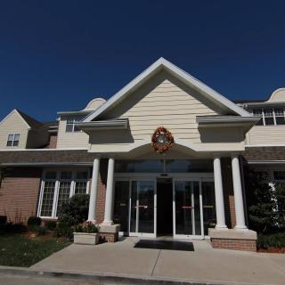 The image shows the entrance of a building with columns and a peaked roof against a clear blue sky.