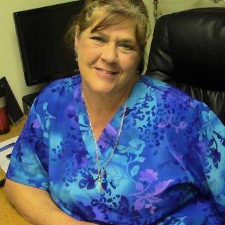 A woman smiles while seated at a desk in an office.