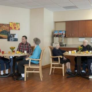 A group of seniors enjoying a meal and conversing in a community dining area.