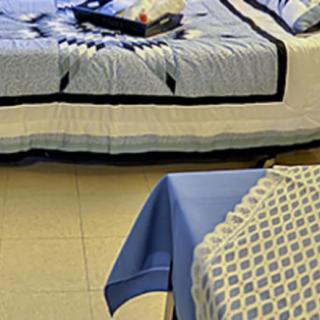 A bedroom with a quilted bedspread and a table covered with a patterned tablecloth.