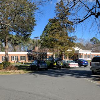 A view of a building surrounded by trees and parked cars on a clear day.