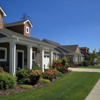 A row of suburban houses with well-maintained lawns and a clear blue sky.
