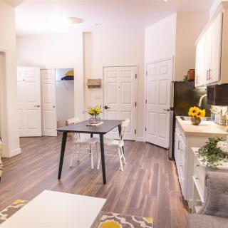 A modern kitchen with a dining table, featuring wood flooring and bright decor.