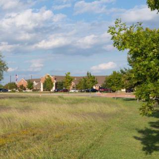 A scenic view of a grassy field with trees and buildings under a partly cloudy sky.