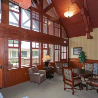 A well-lit living room with wooden ceilings, large windows, and comfortable seating around a central table.