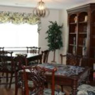 A dining room with a large table, ornate chairs, and a wooden bookshelf.