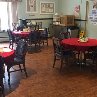 An indoor dining area with multiple tables covered in red tablecloths and surrounded by chairs.