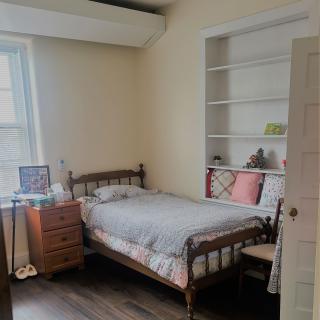 A cozy bedroom with a single bed, bookshelf, and wooden flooring.