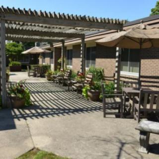 A sunny outdoor patio with seating, a pergola, and umbrellas providing shade.