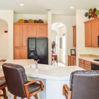 A modern kitchen interior with wooden cabinets, a black refrigerator, and bar stools around the island.