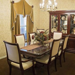 A traditional dining room with a wooden table, upholstered chairs, and a chandelier.