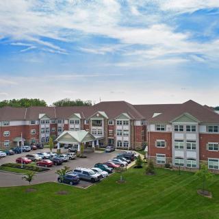 A large residential building with a parking lot and expansive lawn under a partly cloudy sky.