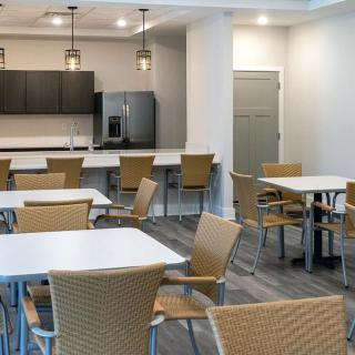 A modern cafeteria with tables and chairs, adjacent to a kitchen area.