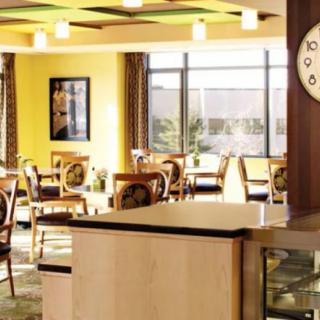 A cozy cafe interior with tables and chairs, featuring large windows and a wall clock.