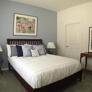 A neatly arranged bedroom featuring a bed with multiple pillows, framed artwork on the walls, and bedside lamps.