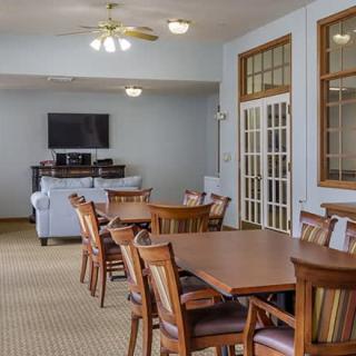 A spacious dining area with wooden tables and chairs, featuring a TV and ceiling fans in a well-lit room.