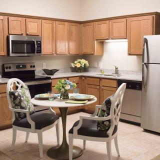 A modern kitchen with wood cabinets, stainless steel appliances, and a small dining area.