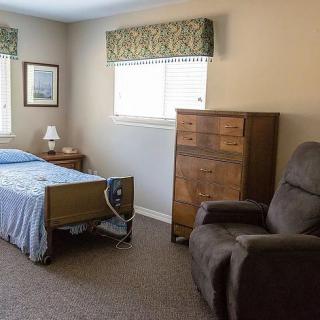A cozy bedroom with a hospital bed, dresser, and recliner chair.
