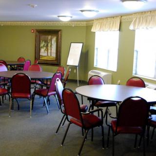An empty meeting room with round tables and red chairs, featuring large windows and a flip chart.