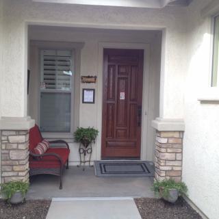 A cozy front porch with a wooden door, a chair, and decorative plants.