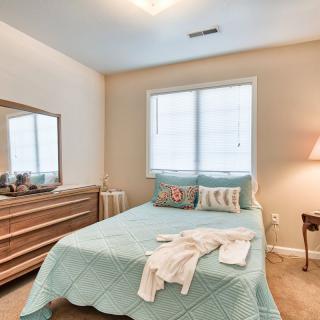 A cozy bedroom featuring a neatly made bed with a light blue comforter, a wooden dresser, and a soft lamp beside the window.