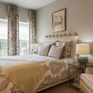 A cozy and well-decorated bedroom featuring patterned bedding, decorative pillows, elegant curtains, and soft lighting from bedside lamps.