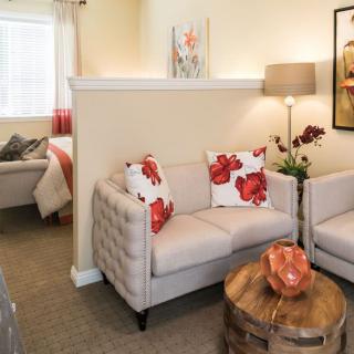 A cozy living room with two tufted sofas, bright floral pillows, a round wooden table, and contemporary artwork.