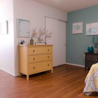 A cozy bedroom featuring a wooden dresser, minimalist decor, and soft pastel accents.
