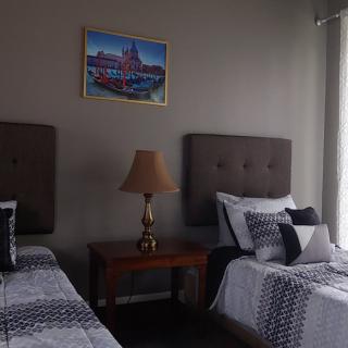 A cozy bedroom featuring two twin beds with patterned bedding and a central lamp on a wooden nightstand under a framed painting.