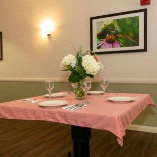An elegantly set dining table with a pink tablecloth, adorned with a floral centerpiece and surrounded by art on the walls.