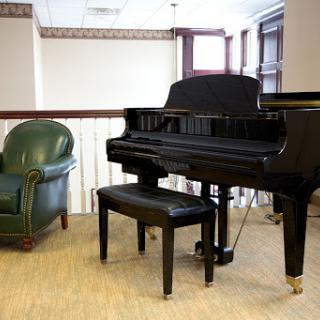 A black grand piano accompanied by a green armchair in a cozy interior setting.