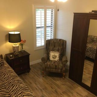 A cozy bedroom featuring a patterned armchair, mirrored wardrobe, and bedside table with a lamp and flowers.