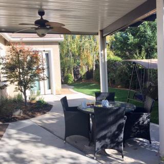 A cozy outdoor patio with a dining set under a covered area, surrounded by greenery.