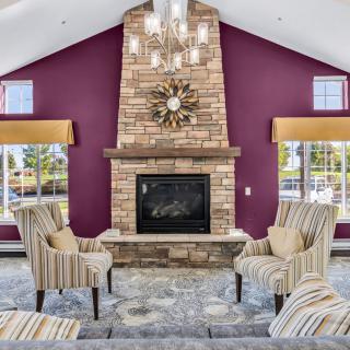 A cozy living room with a central fireplace, surrounded by striped chairs and featuring maroon accent walls and a chandelier.