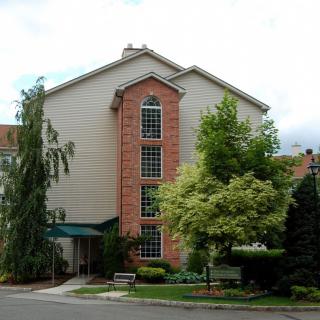 A residential apartment building surrounded by green trees and a small garden.