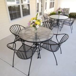 An outdoor patio with metal tables and chairs, featuring a floral centerpiece.